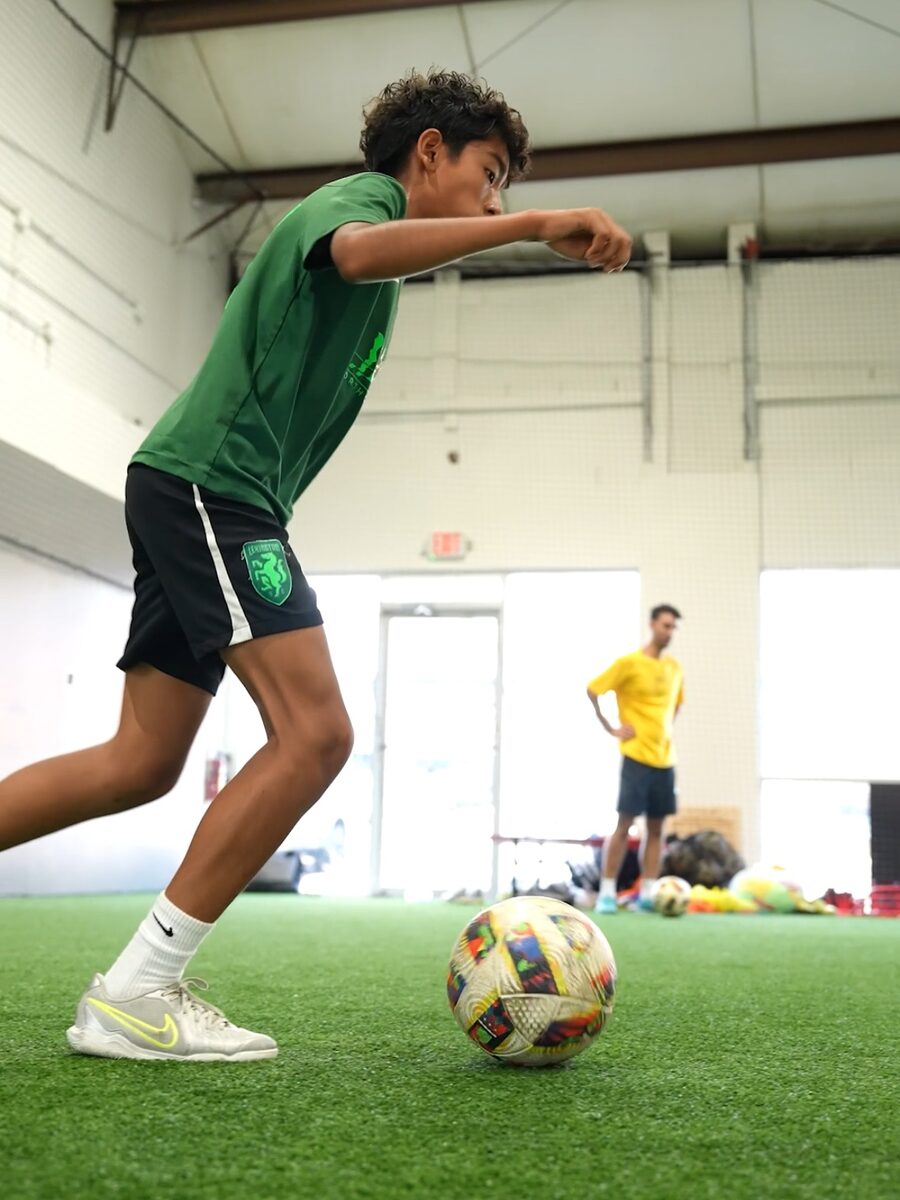 A young player striking the ball on an indoor turf field