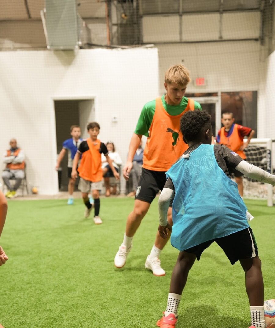 Small-sided game on indoor turf, players in orange and blue bibs
